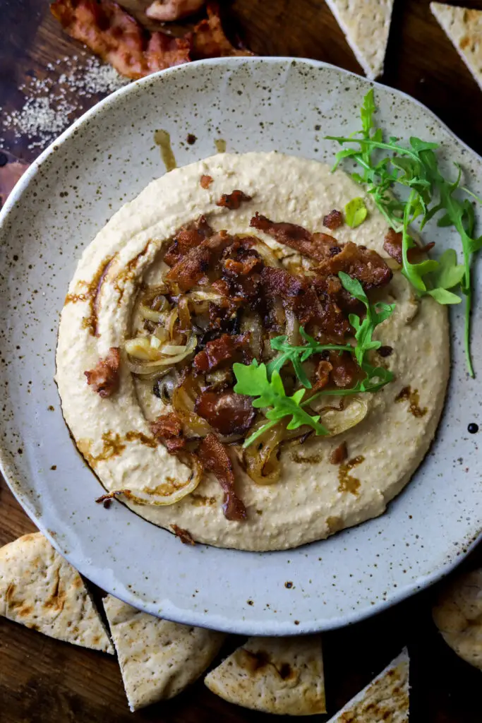 This bacon and caramelized onion hummus and pita bread appetizer. Yum. A different twist on your typical hummus flavors. It's a simple, homemade hummus topped with bacon, sweet, caramelized onion, and a drizzle of balsamic vinegar. This dip is so good I could make a meal out of it.