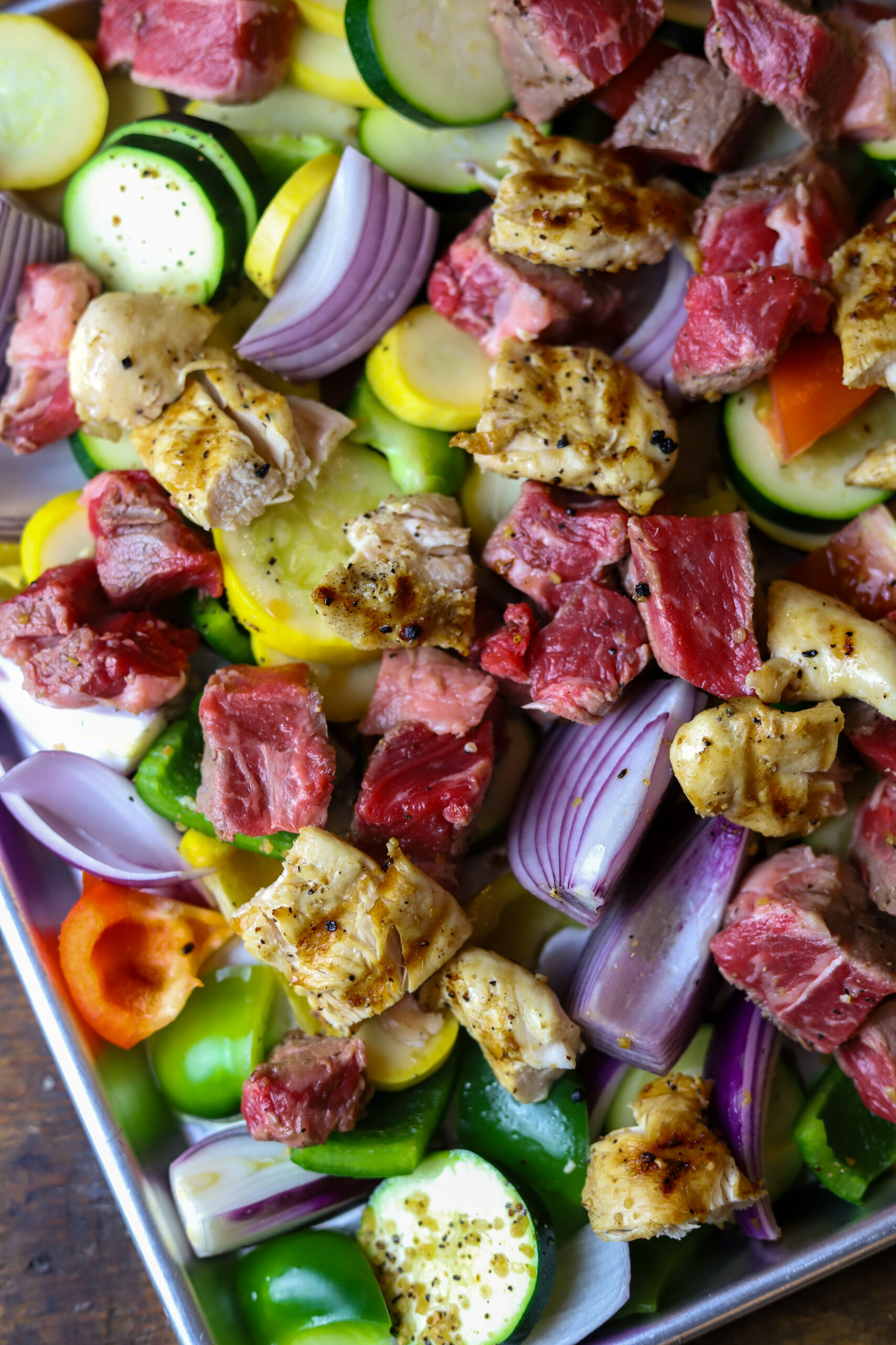 These sheet pan kabobs in the oven are perfect weeknight meal. So, we’re really not re-inventing the wheel here with this recipe. There’s not much to it. First, you’re going to sauté some steak until it’s seared on the outside and then fully cook some chicken. Cut them into pieces and put them on a sheet pan with various vegetables of your choice. I love onions and squash and peppers. Give it all a good douse of olive oil and seasoning and bake for around 20 minutes until vegetables are soft and meat is cooked in the center. This recipe is easy, quick and mess-free.