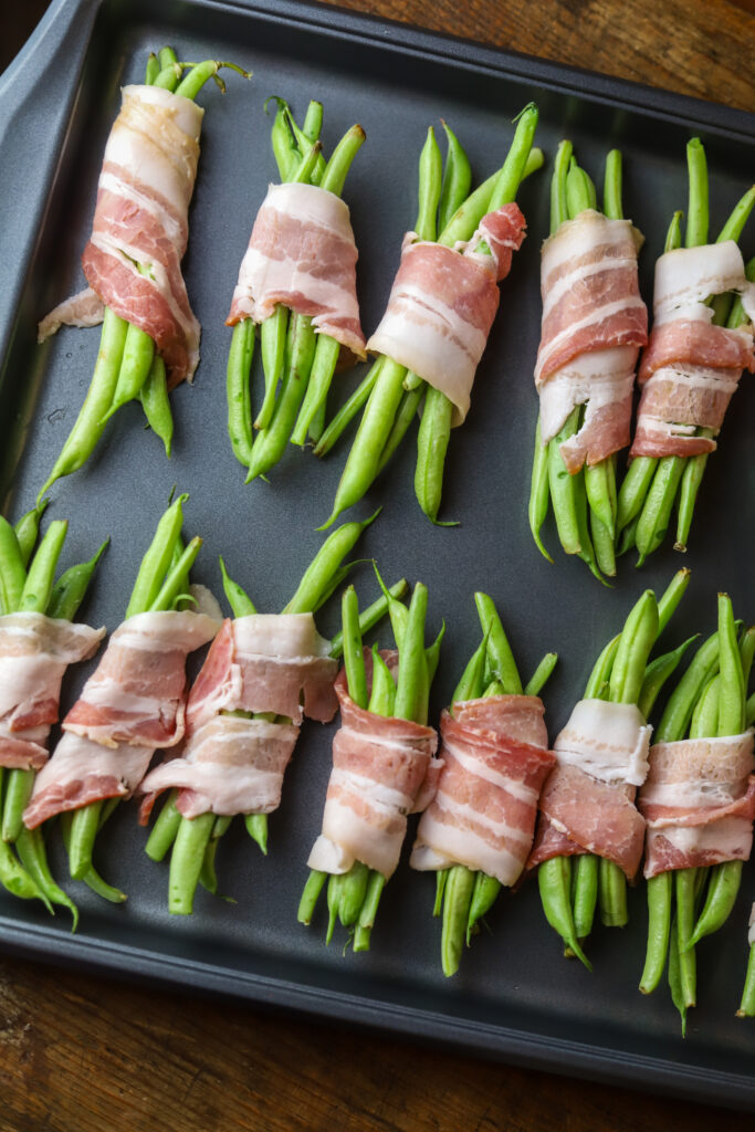 Ok y'all. These zesty Italian bacon wrapped green beans. Simplest, easiest and most delicious side veggie. You'll take some fresh green beans, make a little bundle, wrap them in bacon, then top with a few seasonings, brown sugar, and zesty Italian salad dressing. Bake and that's it. So simple and so delicious!