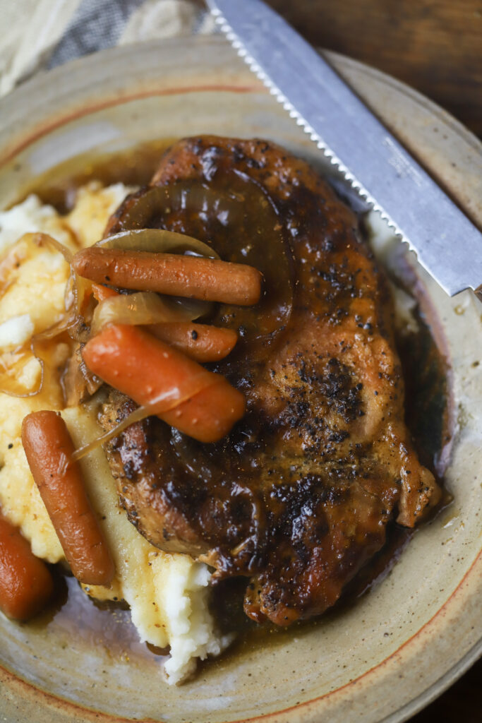 I love these bone-in smothered crockpot pork chops. These are such an easy and delicious comfort food. I started by searing my porkchops in a skillet then added them to my crockpot with some gravy mix, a can of gravy, and some beef consommé. Add some veggies like onions and carrots to complete it. This recipe tastes best over rice or mashed potatoes. You can't beat this comfort dish.