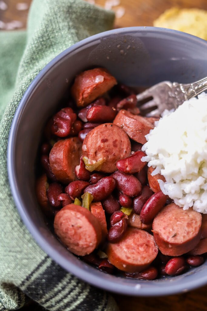 You'll love this easy crockpot red beans and rice. This is the easiest comfort food. You'll need some canned red kidney beans, smoked sausage, some Cajun holy trinity, and of a few seasonings. Let it slow cook all day on high. Serve it with white rice and that's it. This is perfect for a crowd or just as an easy dinner at home. 