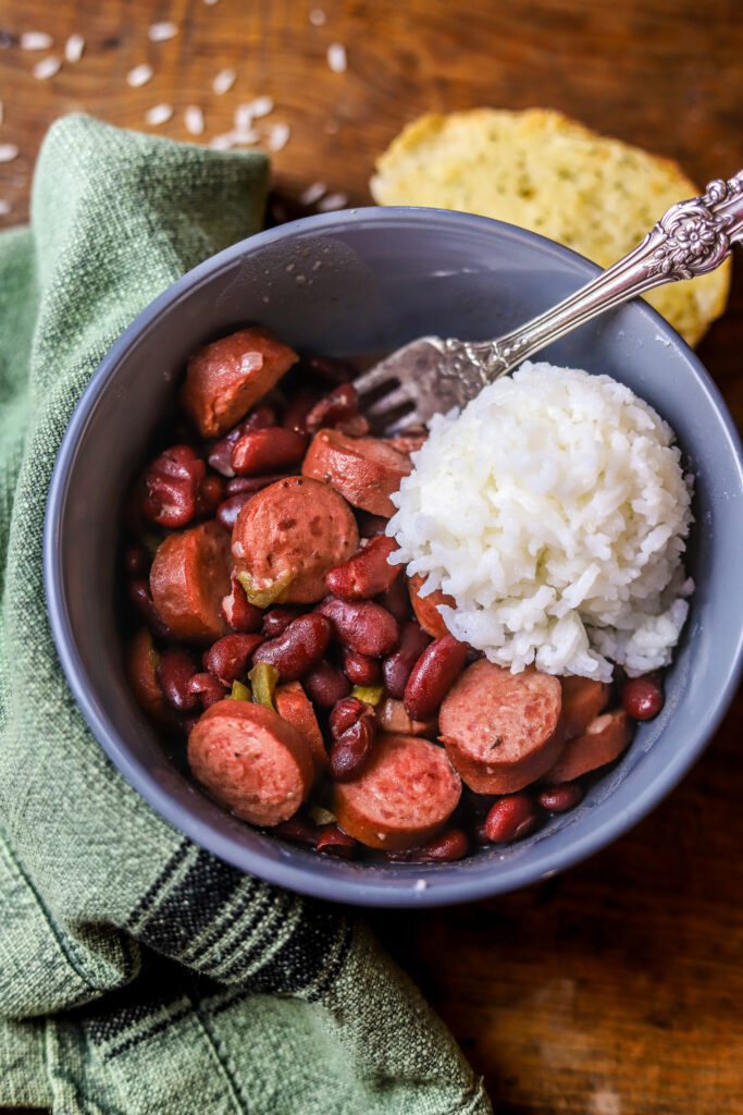 You'll love this easy crockpot red beans and rice. This is the easiest comfort food. You'll need some canned red kidney beans, smoked sausage, some Cajun holy trinity, and of a few seasonings. Let it slow cook all day on high. Serve it with white rice and that's it. This is perfect for a crowd or just as an easy dinner at home. 